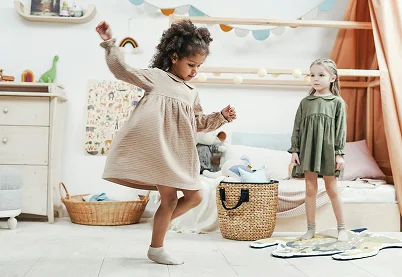Two young girls in dresses playing and dancing in a bright, modern playroom or child therapy space.