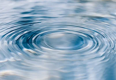 Gentle circular water ripples on a calm blue surface representing the ripple effect of complex trauma healing.