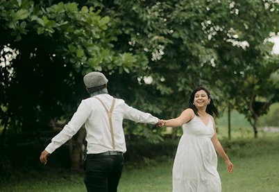 Happy couple holding hands and walking through a lush green park representing healthy partnership and relationship therapy.