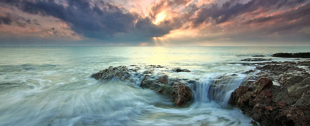 Ocean water flowing over rocks at sunset with sunbeams breaking through clouds, symbolizing hope and recovery from depression.