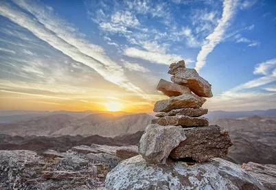 Stacked rock cairn on a mountain peak at sunset representing stability and balance after divorce.