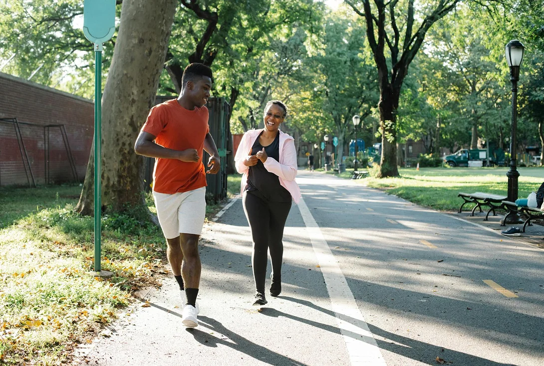 A man and woman jogging and laughing in a sunny park, representing active coping and community support during divorce recovery.