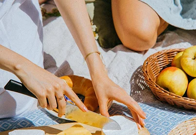 Close-up of a person cutting Brie cheese during a bright outdoor picnic, symbolizing food freedom and eating disorder recovery.