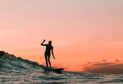 Silhouette of a surfer riding a wave at sunset during golden hour