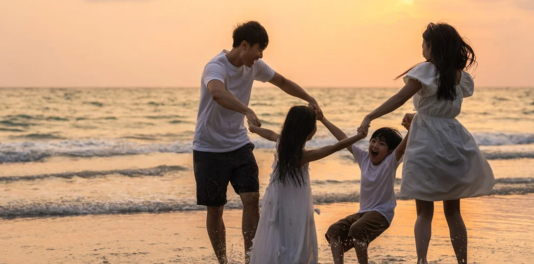 Happy family of four holding hands and playing in the ocean waves at sunset