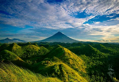 Vast green mountain range with a central volcanic peak under a cloudy sky, representing the journey of grief recovery.