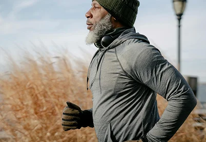 Side profile of a mature man with a gray beard jogging outdoors in athletic gear and a beanie