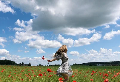 Woman in a floral dress spinning joyfully in a poppy field, representing the emotional wellness and renewal of new parents.
