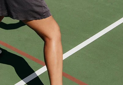 Close-up of an athlete's leg and shadow on a green tennis or basketball court with white lines