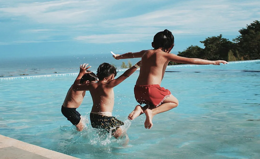 Children jumping into swimming pool and splashing water on a sunny day