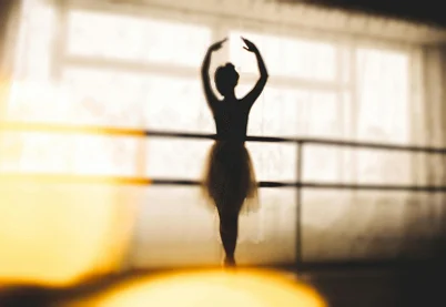 ilhouette of a ballerina in a tutu practicing at a dance bar, representing play-based therapy and creative expression.