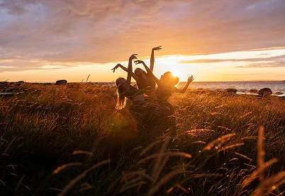 Three people dancing in a field of tall grass at sunset, symbolizing somatic healing and recovery from PTSD.