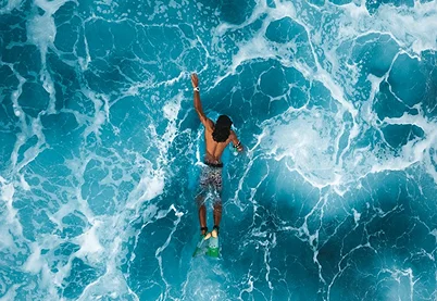 Aerial top-down view of a person swimming through bright blue ocean water with white sea foam