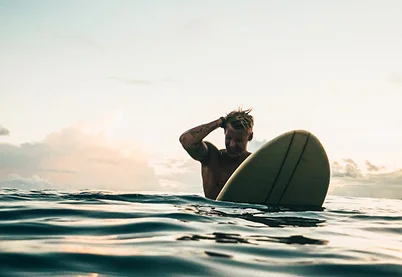 Surfer sitting on a surfboard in the ocean at sunset with gentle waves in the foreground