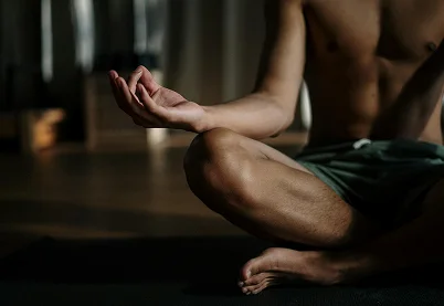 Close-up of a person sitting in a cross-legged meditation pose with hands in a mudra position on a yoga mat