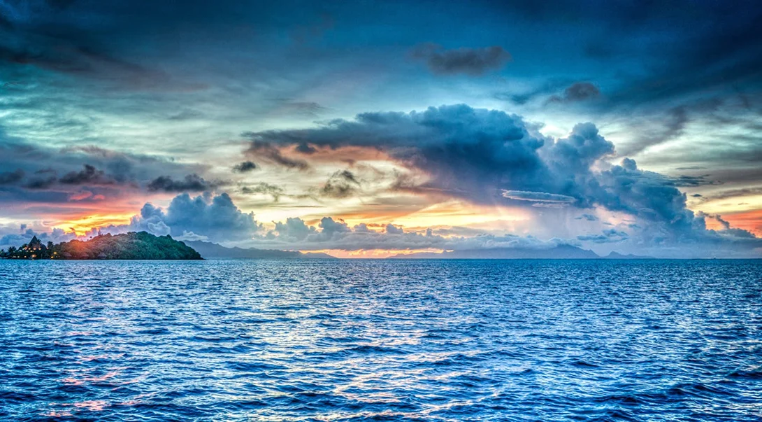 Tropical island landscape at sunset with vibrant blue ocean water and dramatic storm clouds in the sky