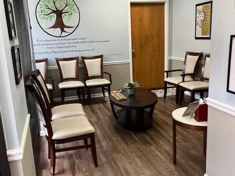 A cozy, well-lit waiting room or office featuring a gray sofa, warm lamps, and decorative wall frames.